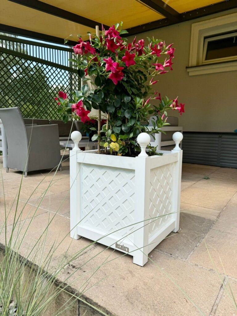 Weißer Pflanzkübel mit roten Blumen auf einer Terrasse