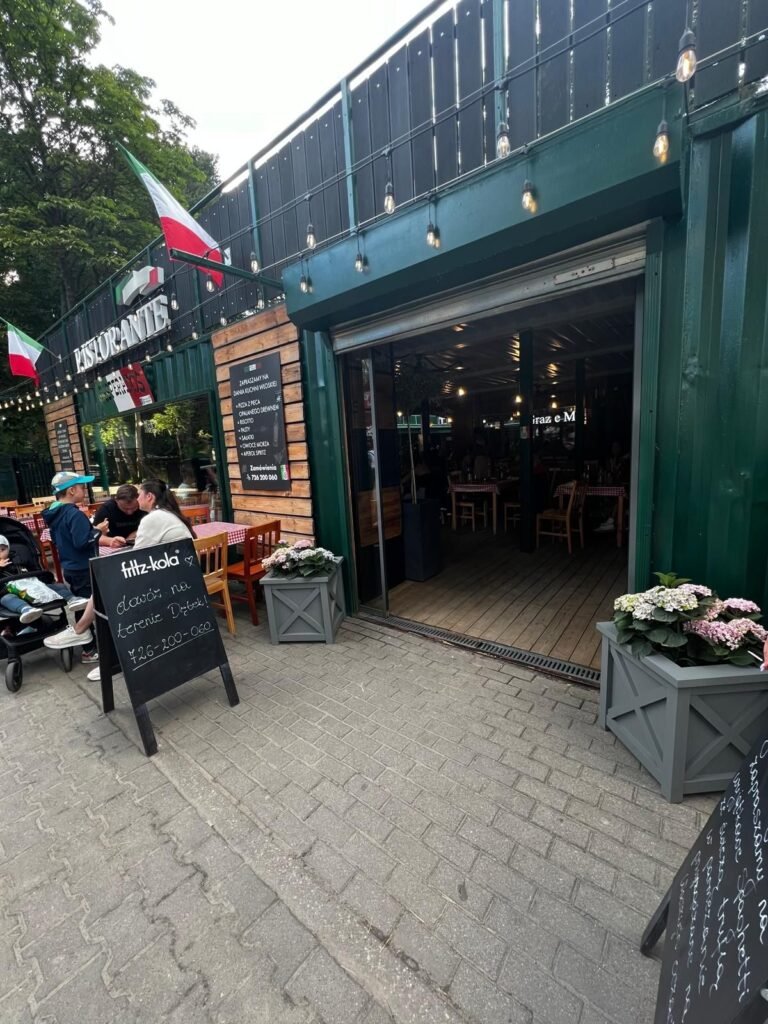 Graue Pflanzkübel mit Blumen vor einem Restaurant mit Außenterrasse
