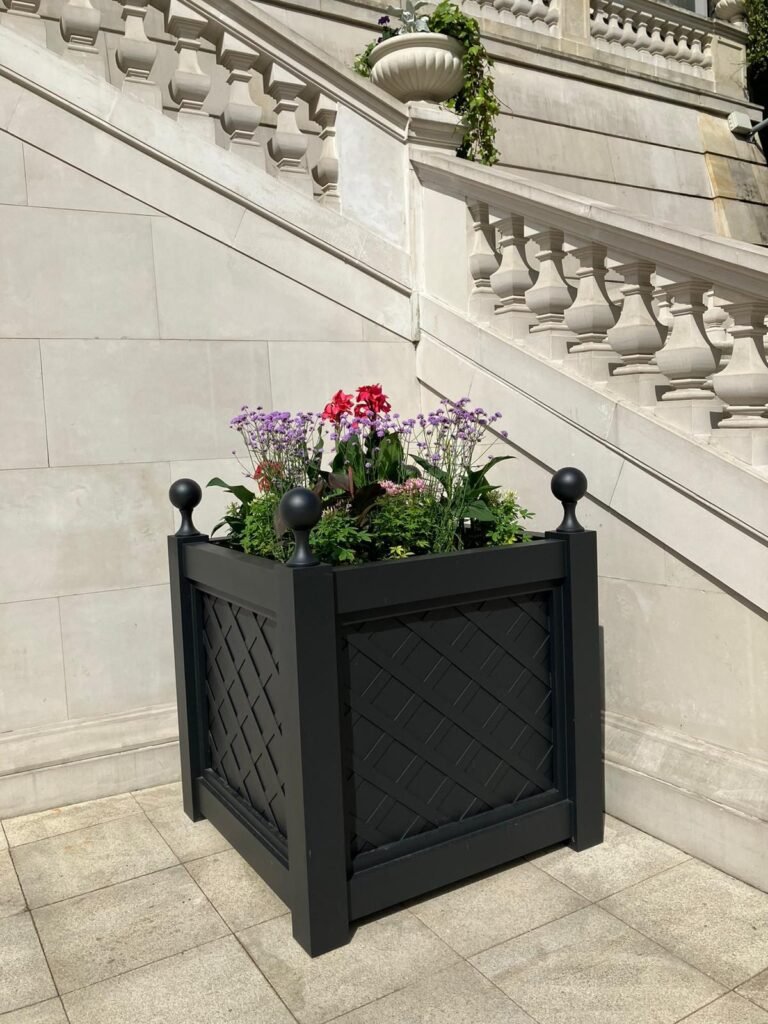 Ein schwarzer dekorativer Pflanzkübel mit Blumen steht vor einer klassischen Steintreppe mit Balustrade an einem eleganten Gebäude